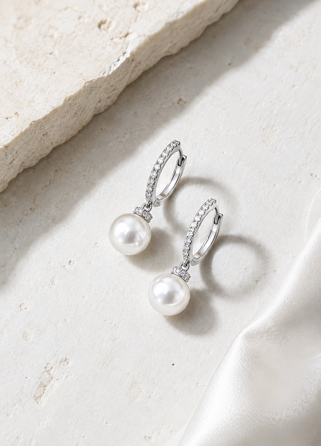 Silver CZ hoop earrings with pearl drops displayed on a premium neutral background.
