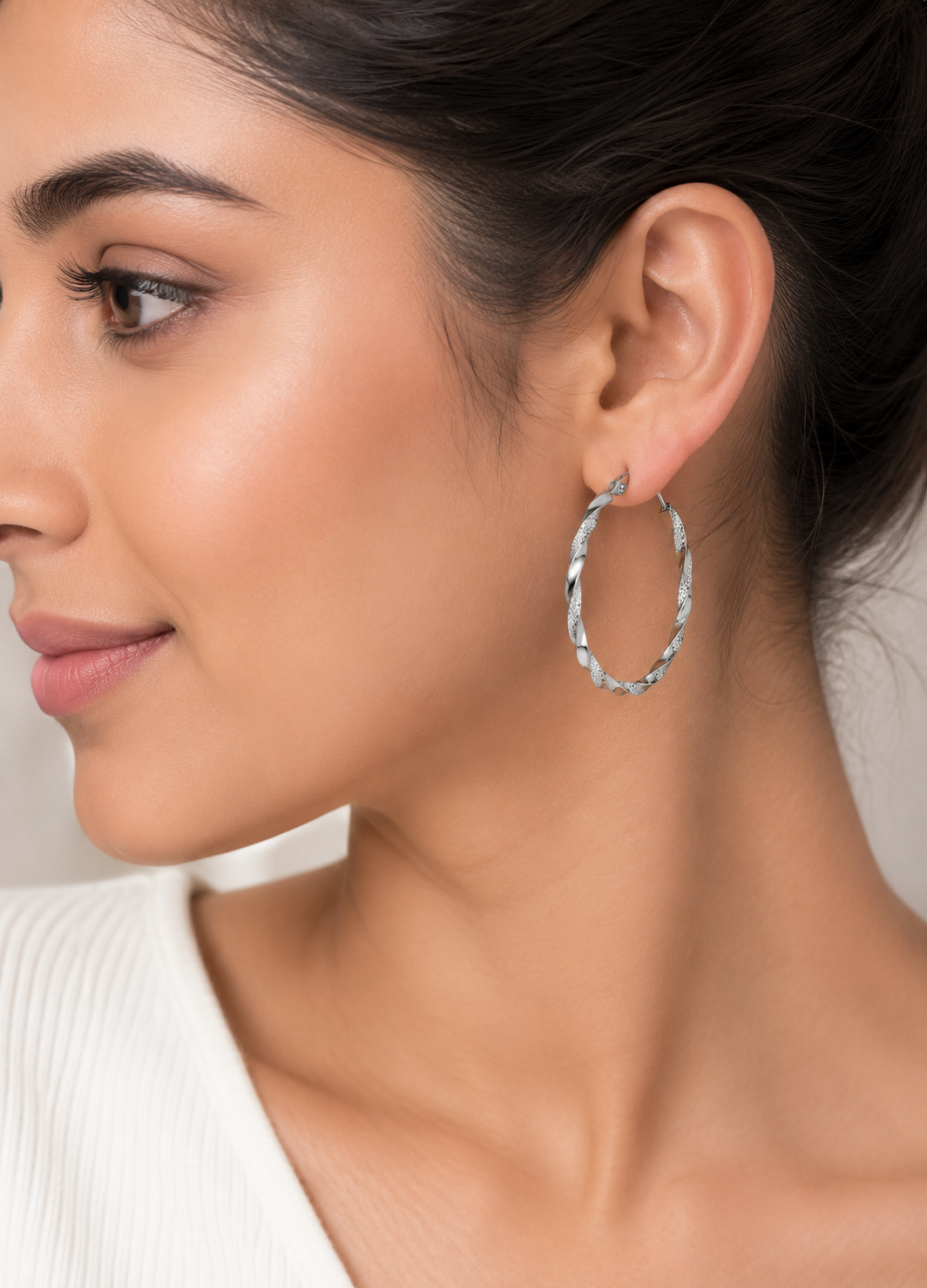 Woman wearing Orelva Celeste twisted silver hoop earrings with elegant textured spiral design.