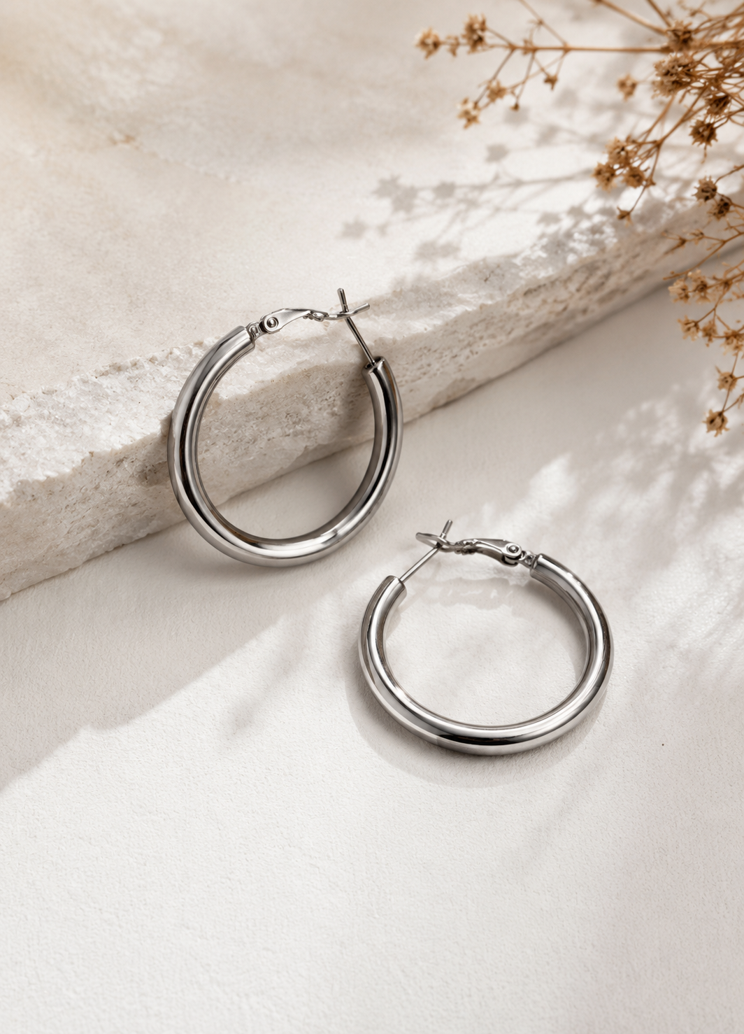 Pair of Orelva silver hoop earrings displayed on a premium neutral background.