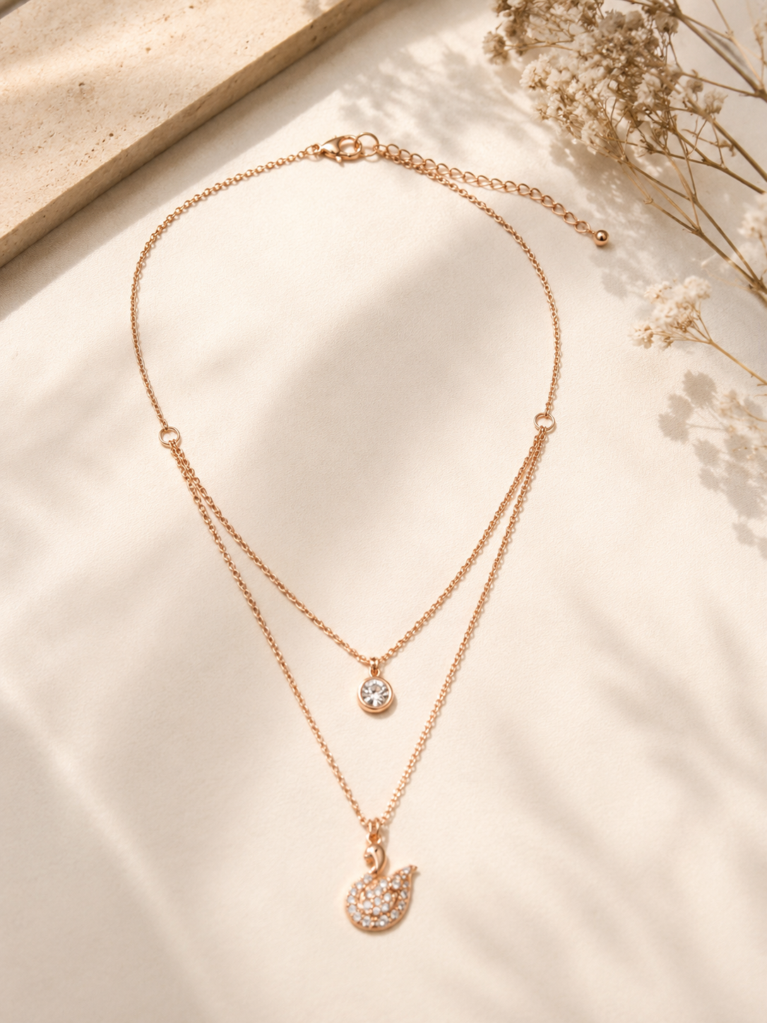 Elegant rose gold layered necklace featuring a crystal solitaire and swan pendant.