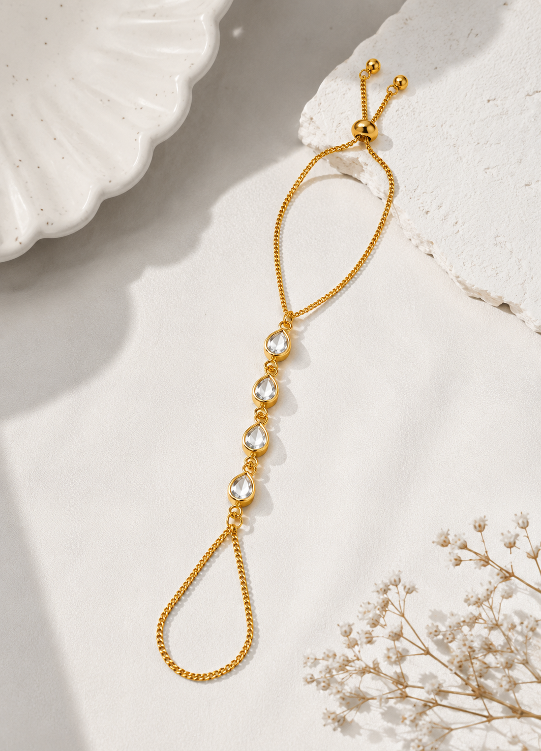 Orelva gold hand harness bracelet with teardrop crystal stones displayed on a decorative flat lay.