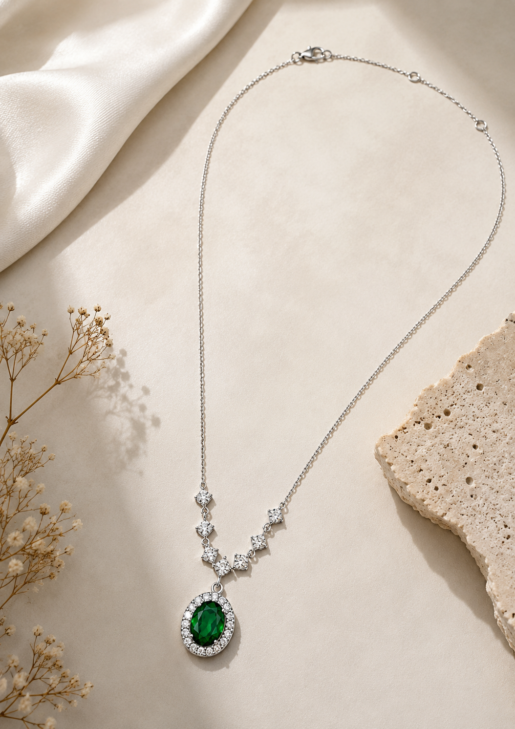 Elegant sterling silver pendant necklace featuring an emerald green gemstone surrounded by a shimmering halo.