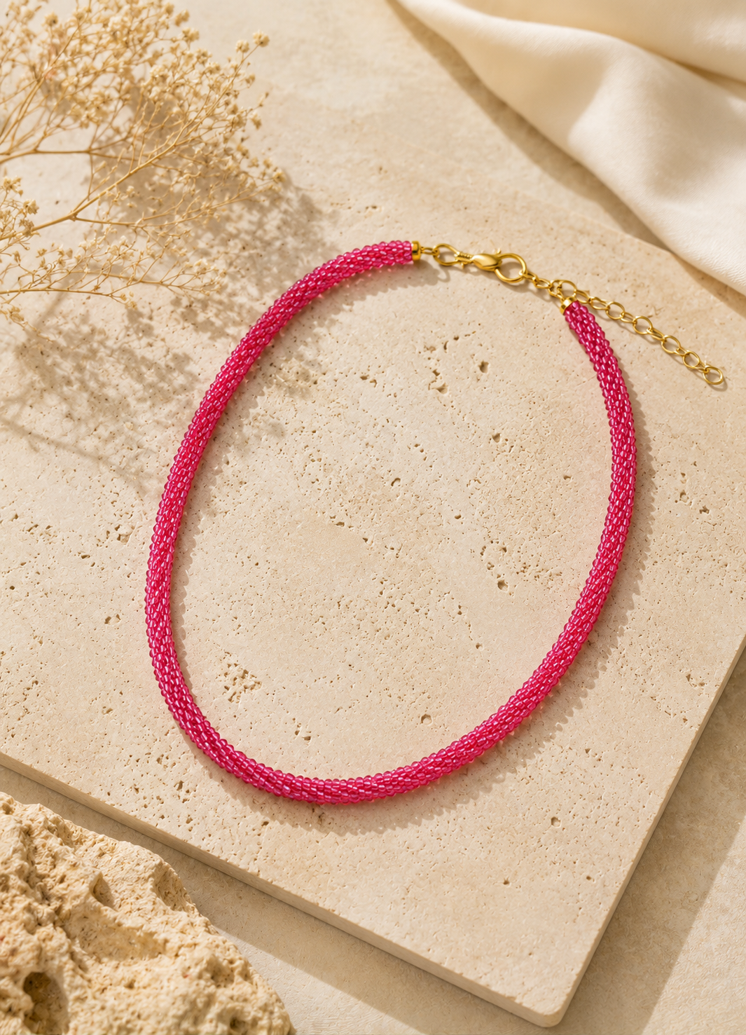 Orelva pink handcrafted beaded necklace displayed on neutral stone background