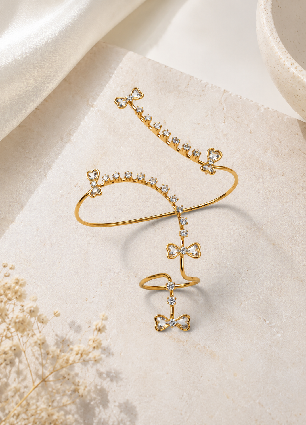 Gold bow crystal hand harness bracelet ring displayed on a premium neutral background.