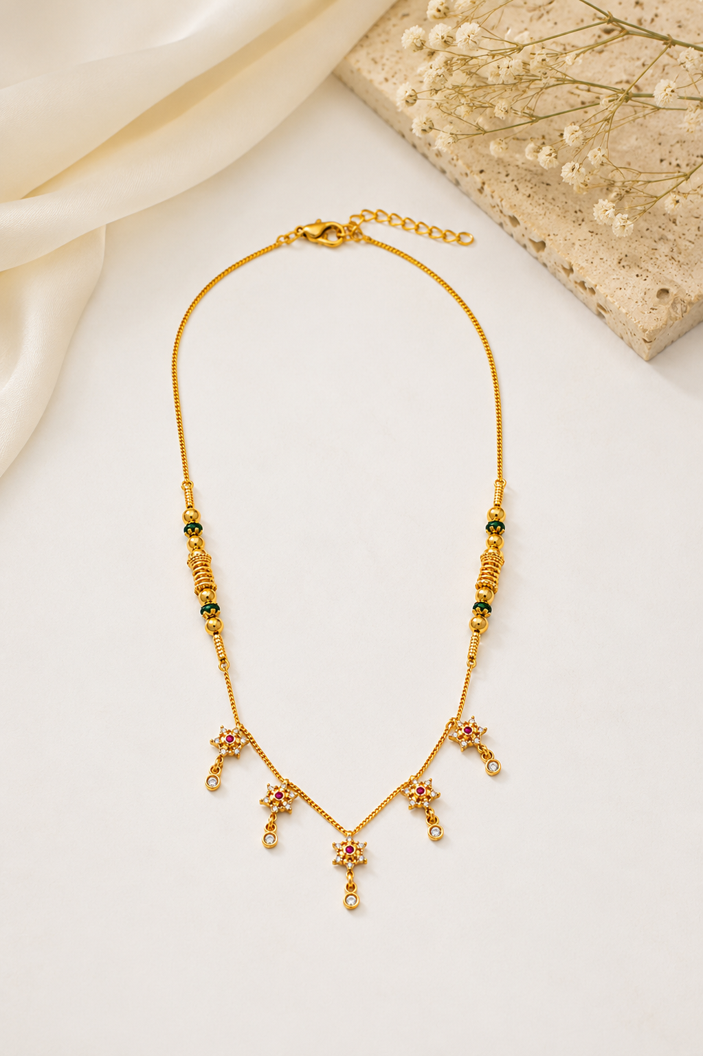 Gold-plated ORELVA Aarohi floral mangalsutra necklace displayed on a premium white fabric background.