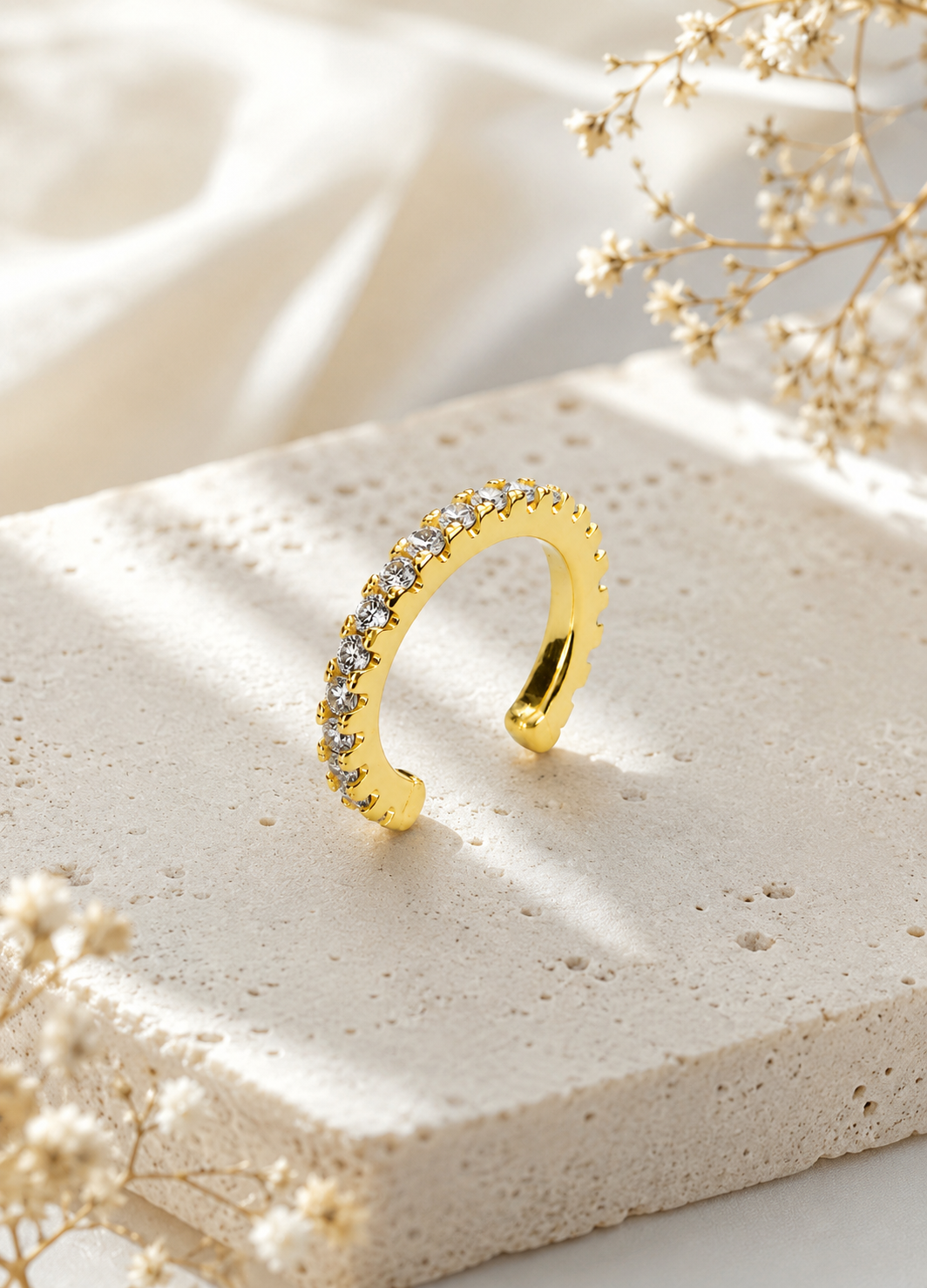 Orelva Aurora gold plated crystal ear cuff displayed on a premium stone background.