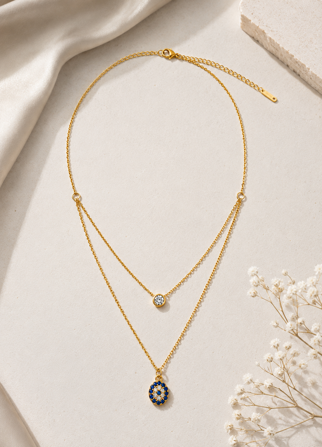 Elegant ORELVA gold layered necklace featuring a blue evil eye pendant and crystal accent.