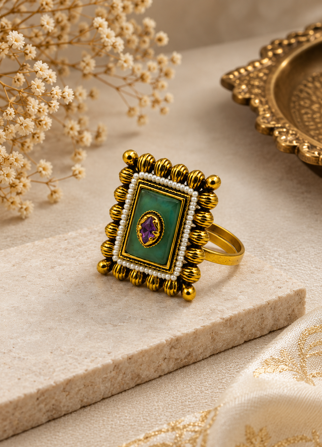 Close-up of Orelva adjustable gold-tone statement ring featuring an emerald green centerpiece, pearl border, and purple accent stone.