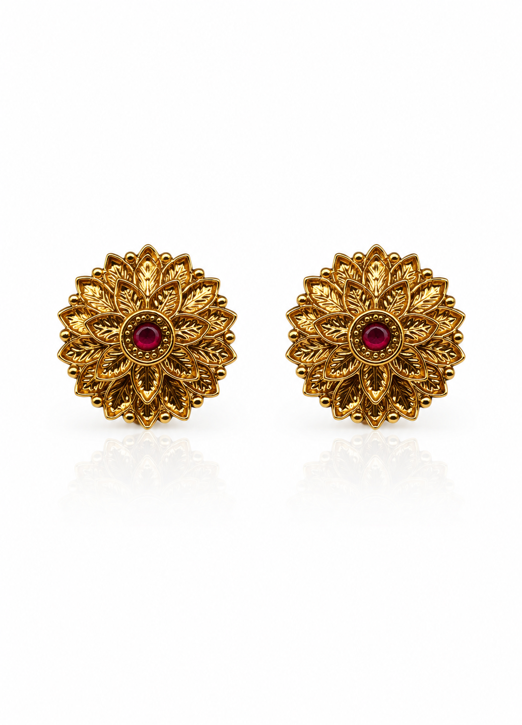 A pair of gold-toned floral stud earrings with a small round red gemstone in the center, displayed on a clean white background with a soft reflection below.