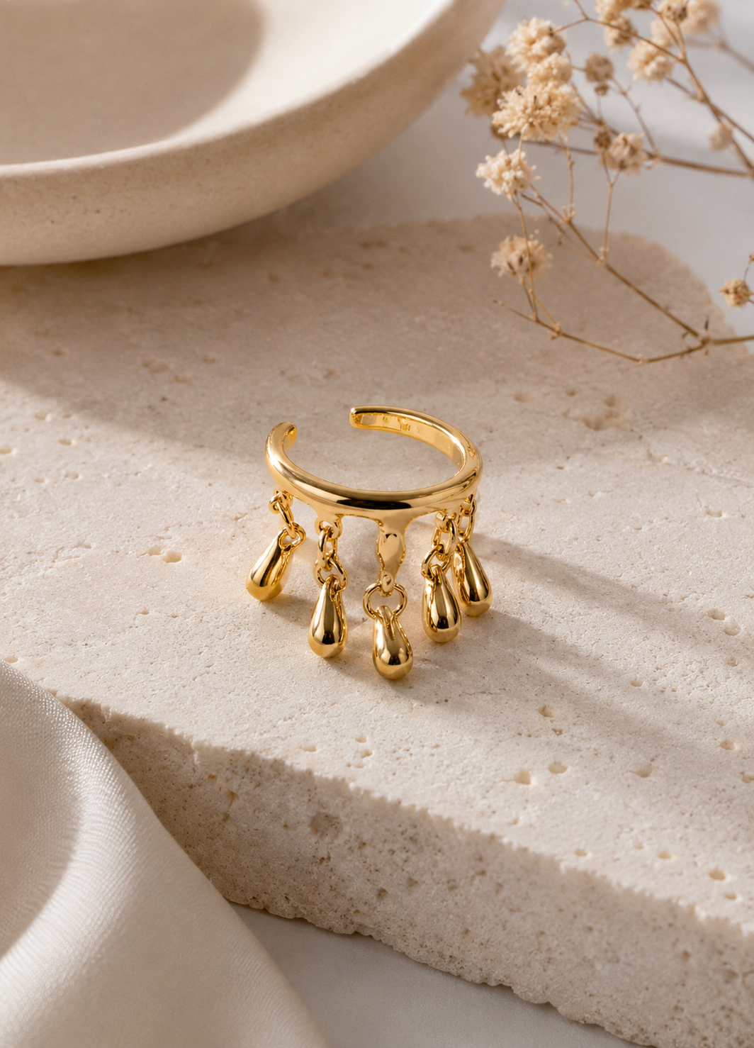 ORELVA gold tone ear cuff with dangling drops displayed on a neutral stone background.