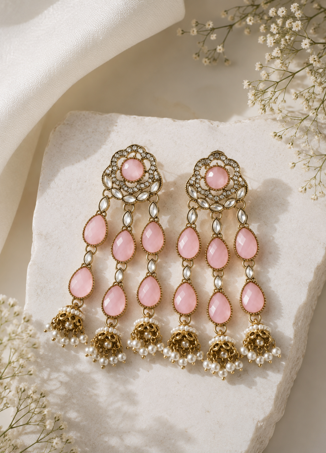 Gold-plated blush pink Polki jhumka earrings with pearl drops displayed on a premium marble background.
