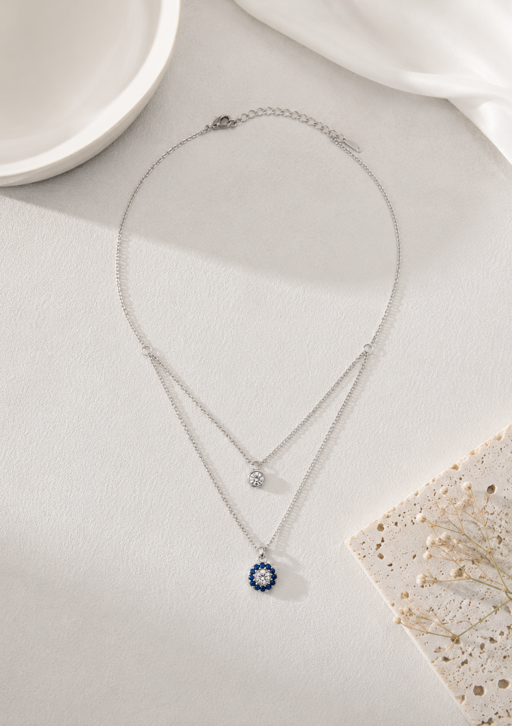 Silver tone layered necklace featuring a blue evil eye pendant and sparkling crystal charm